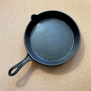 May include: A black cast iron skillet with a long handle. The skillet has a smooth, black surface and a slightly raised lip around the edge.