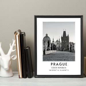 May include: Black and white photograph of Charles Bridge in Prague, Czech Republic. The photo shows the bridge with its iconic towers and statues, and the city in the background. The text "PRAGUE" and "CZECH REPUBLIC" is printed below the image, along with the coordinates "50.0755° N, 14.4378° E".