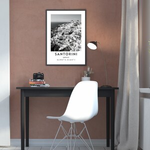 Puede incluir: Fotograf&iacute;a en blanco y negro de Santorini, Grecia. La imagen muestra una ciudad con edificios blancos agrupados en un acantilado. El texto "SANTORINI" est&aacute; impreso en blanco en la parte inferior de la imagen, junto con las coordenadas "36.3932&deg; N, 25.4615&deg; E".