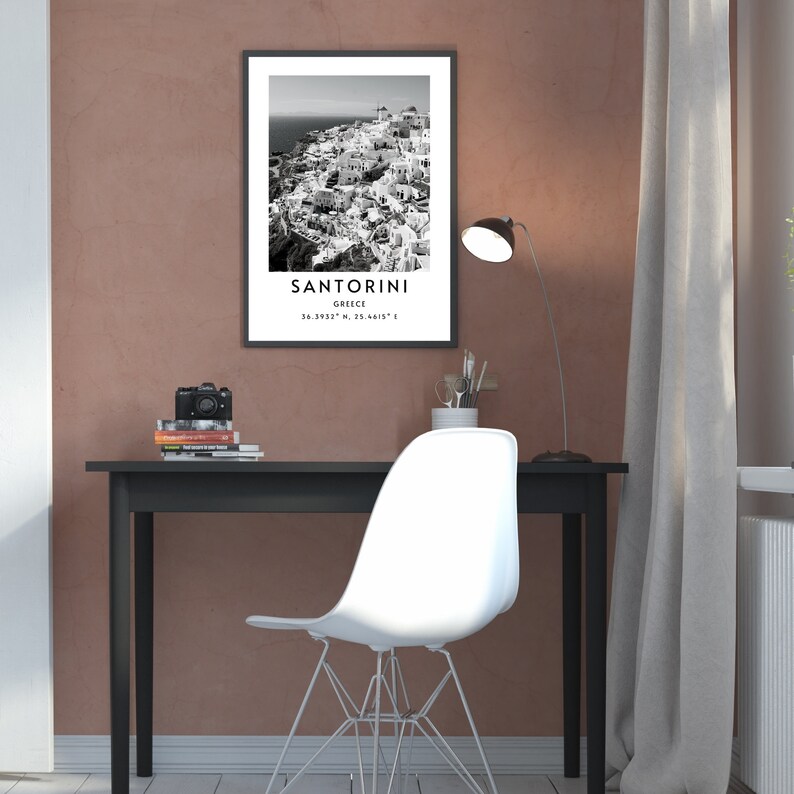 Puede incluir: Fotograf&iacute;a en blanco y negro de Santorini, Grecia. La imagen muestra una ciudad con edificios blancos agrupados en un acantilado. El texto "SANTORINI" est&aacute; impreso en blanco en la parte inferior de la imagen, junto con las coordenadas "36.3932&deg; N, 25.4615&deg; E".