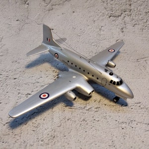 May include: A silver model airplane with red, white, and blue markings. The airplane has a round window and a tail with a red, white, and blue flag. The model is on a gray textured surface.