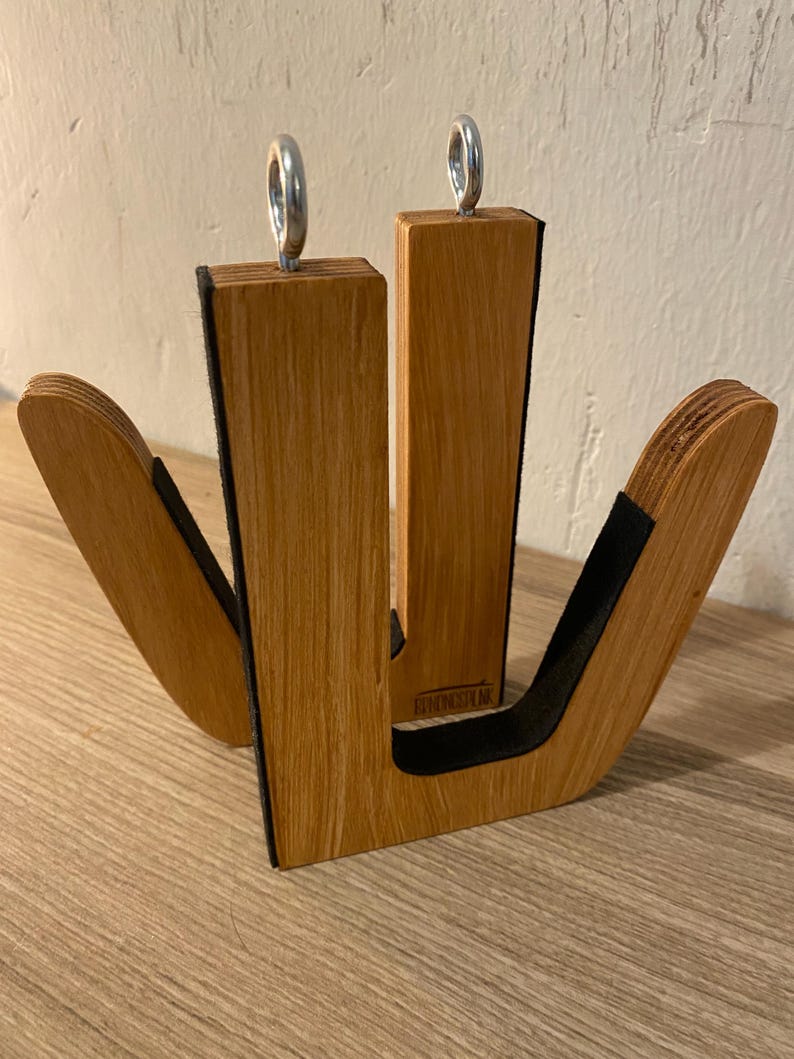 May include: Wooden surfboard rack with a natural wood grain finish. The rack has two vertical supports with metal rings at the top and curved arms with black padding. The rack is designed to hold surfboards.