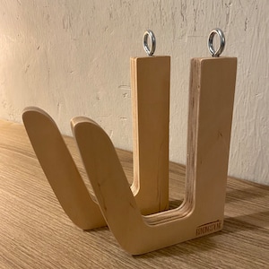 May include: A light-colored wooden surfboard rack with a U-shaped design. The rack has two curved arms and two vertical supports, each topped with a metal ring. The text "BENDINGSPLNK" is visible on the base.