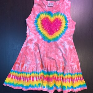 May include: Pink tie-dye sleeveless dress with a rainbow heart design and a yellow, blue, and green tie-dye band around the bottom. The dress has a size tag that says "Size 6".
