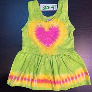 May include: Green tie-dye sleeveless dress with a pink heart design and a ruffled hem. The dress has the text "SIZE 4T" on a white tag.