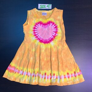 May include: A yellow tie-dye sleeveless dress with a pink heart design. The dress has a size tag that says "Size 4T".