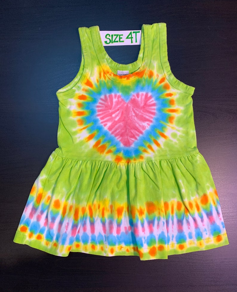 May include: Green tie-dye sleeveless dress with a pink heart design. The dress has a ruffled hem and says "SIZE 4T" on the tag.