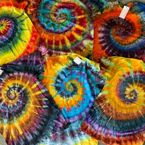 May include: Six tie-dye t-shirts in various shades of yellow, orange, blue, green, and purple with a spiral pattern.