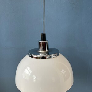 May include: A white dome-shaped pendant light with a chrome finish. The light is suspended from a black cord.