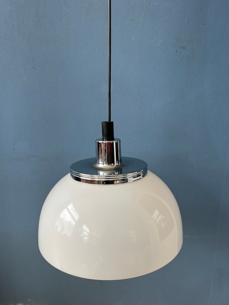 May include: A white dome-shaped pendant light with a chrome finish. The light is suspended from a black cord.