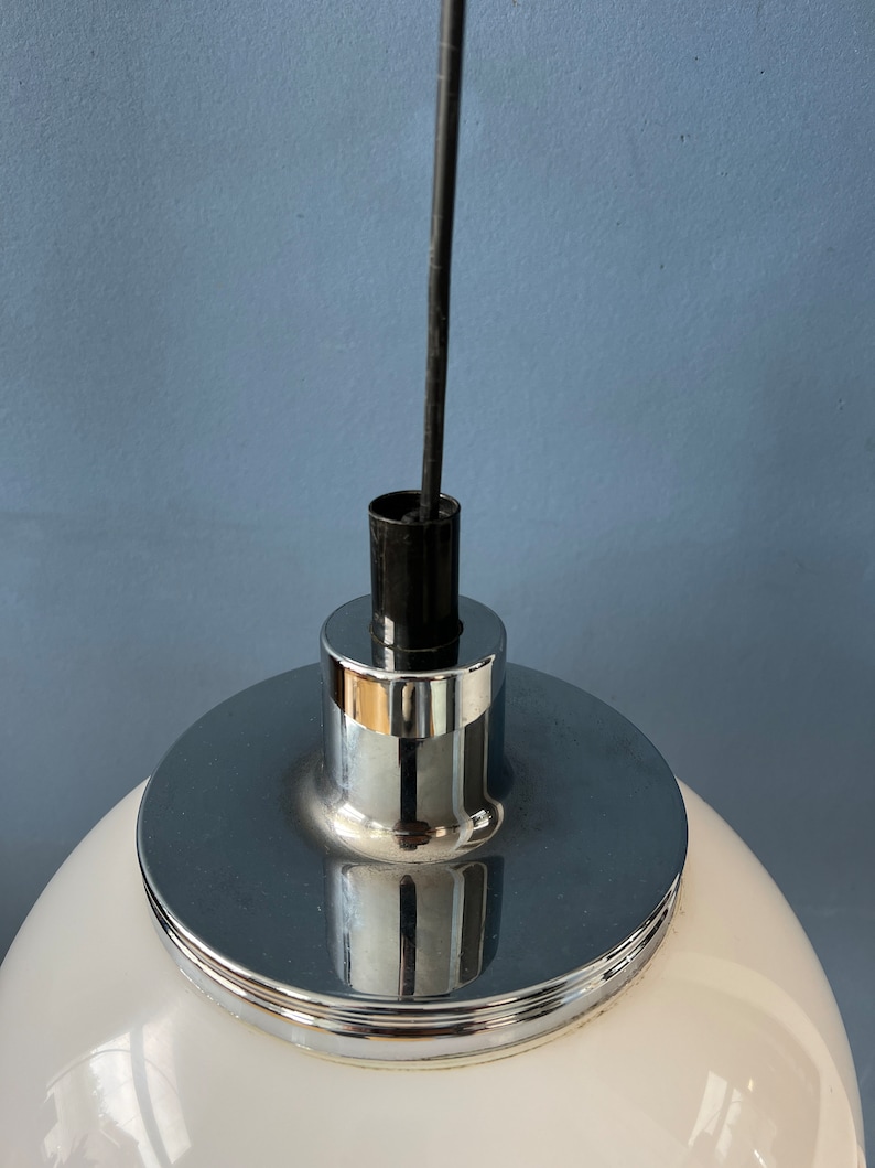 May include: Close-up of a white globe pendant light fitting with a chrome metal base and a black wire.