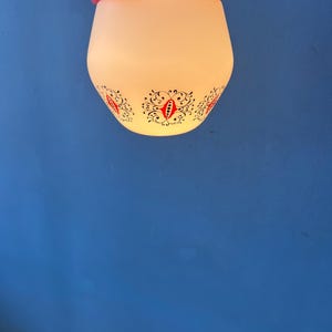 May include: A pendant light fixture featuring a frosted white glass shade with a repeating black and red floral scroll pattern. The shade is attached to a bright red rectangular ceiling mount with a black electrical cord extending from the side.