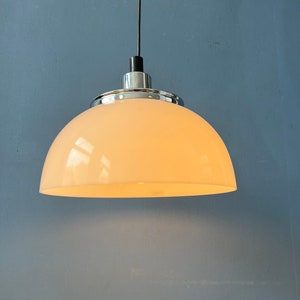 May include: A white dome-shaped pendant light fixture with a chrome finish hangs from a black cord against a blue wall.