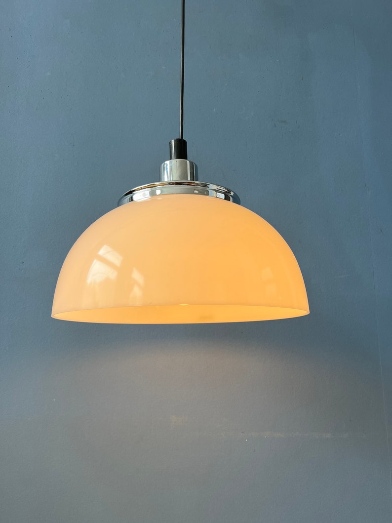May include: A white dome-shaped pendant light fixture with a chrome finish hangs from a black cord against a blue wall.