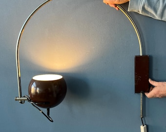 May include: A brown and chrome wall-mounted lamp with a spherical shade and a curved arm. The lamp is plugged into a wall outlet and has a switch. The lamp is held by a person.