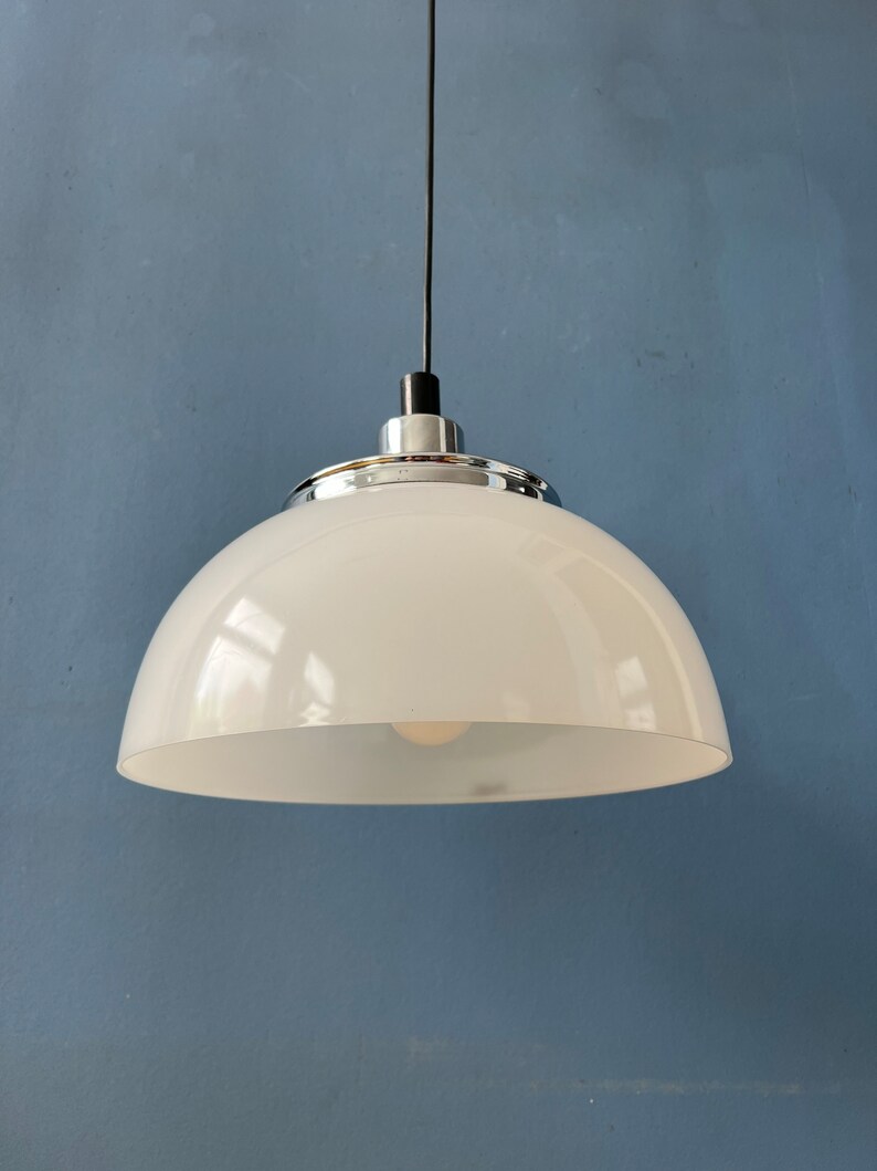 May include: A white dome-shaped pendant light fixture with a chrome trim hangs from a black cord against a blue wall.