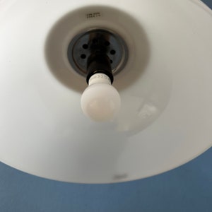 May include: White ceiling light fitting with a white glass shade and a black electrical cord. The fitting has a silver metal base with a series of small holes. The light bulb is a standard incandescent bulb.