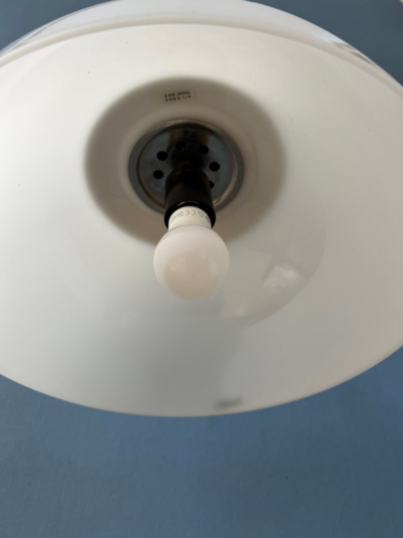 May include: White ceiling light fitting with a white glass shade and a black electrical cord. The fitting has a silver metal base with a series of small holes. The light bulb is a standard incandescent bulb.