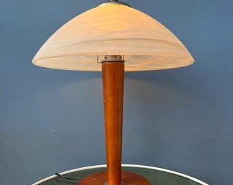 Puede incluir: Una pantalla de lámpara de vidrio blanco con una base de madera. La pantalla tiene forma de hongo y tiene un acabado blanco texturizado. La base es de madera marrón oscura y tiene forma cilíndrica.