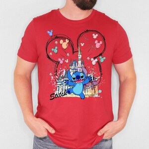 May include: Red t-shirt featuring a cartoon illustration of Stitch from Lilo & Stitch. The design includes a castle, Mickey Mouse ears, and the word "Stitch". The shirt is a crew neck style.