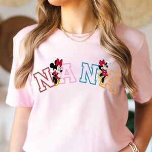 May include: Pink t-shirt with a colorful "NANA" graphic featuring two Mickey Mouse characters.