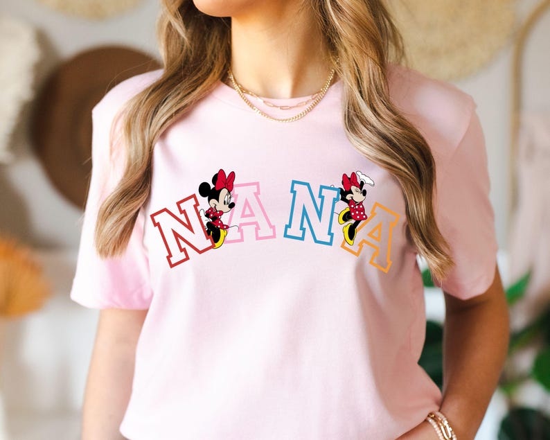 May include: Pink t-shirt with a colorful "NANA" graphic featuring two Mickey Mouse characters.