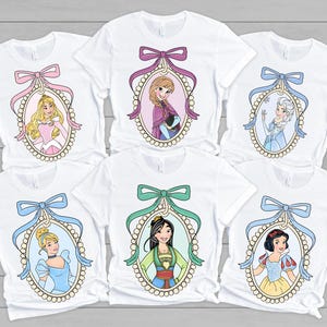 以下が含まれることがあります： 真珠の枠の中に異なるディズニーのプリンセスが描かれた白いTシャツが6枚。各プリンセスはカラフルなリボンで囲まれています。プリンセスはオーロラ、エルサ、ムーラン、シンデレラ、アリエル、白雪姫です。