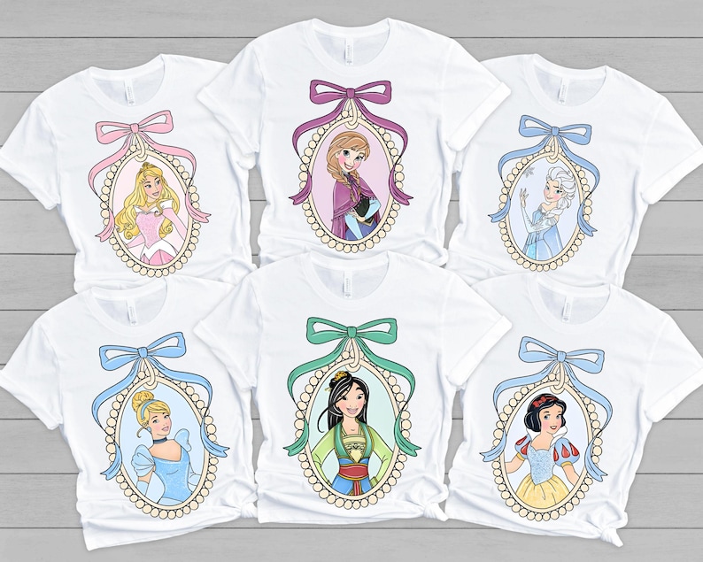 以下が含まれることがあります： 真珠の枠の中に異なるディズニーのプリンセスが描かれた白いTシャツが6枚。各プリンセスはカラフルなリボンで囲まれています。プリンセスはオーロラ、エルサ、ムーラン、シンデレラ、アリエル、白雪姫です。