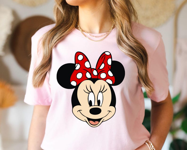 May include: Pink t-shirt with a graphic of Minnie Mouse wearing a red bow with white polka dots.