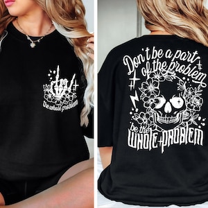 Könnte beinhalten: Schwarzes T-Shirt mit einem weißen Totenkopf und einem floralen Design auf der Rückseite. Die Vorderseite des Shirts zeigt eine weiße Skeletthand mit dem Text "Sei nicht Teil des Problems, sei das ganze Problem".