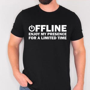 May include: Black t-shirt with the word "OFFLINE" above the phrase "ENJOY MY PRESENCE FOR A LIMITED TIME" in white block letters. The shirt has a crew neck and short sleeves.