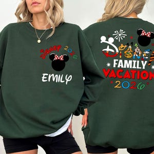 May include: Dark green sweatshirt with "Disney 2026" and a Minnie Mouse design on the front. The name "Emily" is below the design. The back features a "Family Vacation 2026" design with Disney characters and fireworks.