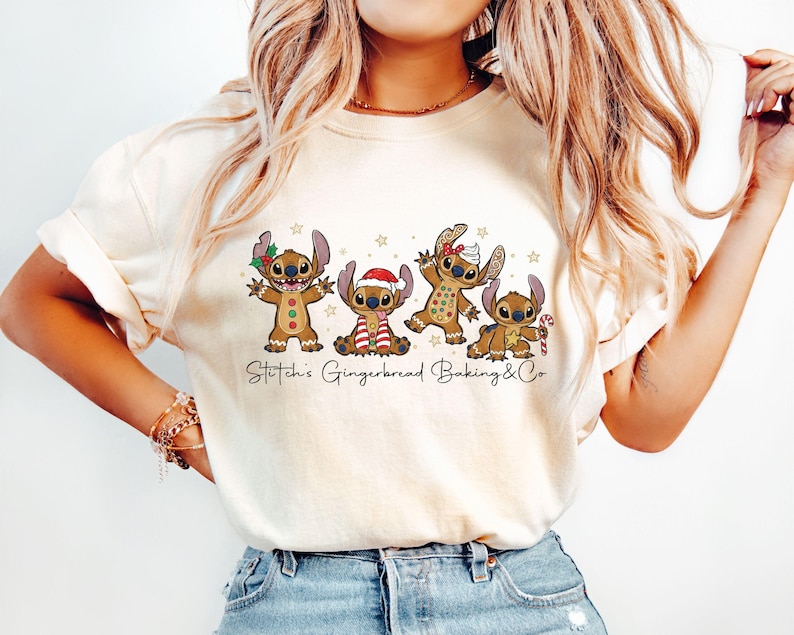 Puede incluir: Camiseta color crema con un gr&aacute;fico festivo de cuatro personajes Stitch vestidos de hombre de jengibre. El dise&ntilde;o incluye un gorro de Pap&aacute; Noel, un bast&oacute;n de caramelo y el texto "Stitch's Gingerbread Baking & Co". La camiseta es de material suave.