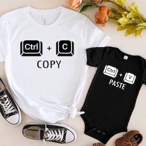 以下が含まれることがあります： 白いTシャツに黒い文字で「Ctrl + C COPY」と書いてあり、黒いボディスーツに白い文字で「Ctrl + V PASTE」と書いてあります。