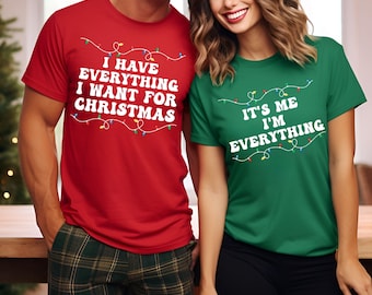 May include: Two t-shirts, one red and one green. The red t-shirt has the text "I HAVE EVERYTHING I WANT FOR CHRISTMAS" in white, with Christmas lights. The green t-shirt says "IT'S ME I'M EVERYTHING".