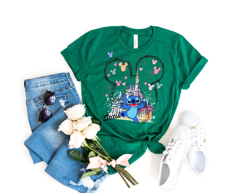 May include: Green t-shirt featuring a graphic of Stitch from Lilo & Stitch in front of a castle, with Mickey Mouse ears and the word "Smile". The shirt is styled with blue jeans, sunglasses, white sneakers, and a bouquet of white roses.