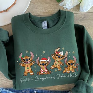 Puede incluir: Una sudadera verde oscuro con un gr&aacute;fico de cuatro personajes de jengibre, con el texto Stitch's Gingerbread Baking & Co. Los personajes tienen poses festivas, con accesorios como un gorro de Pap&aacute; Noel y un bast&oacute;n de caramelo.