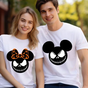 Puede incluir: Dos camisetas blancas con un dise&ntilde;o gr&aacute;fico negro y naranja. Una camiseta presenta un dise&ntilde;o inspirado en Mickey Mouse con un lazo, y la otra tiene un dise&ntilde;o similar sin lazo. El gr&aacute;fico tiene un tema espeluznante de Halloween.