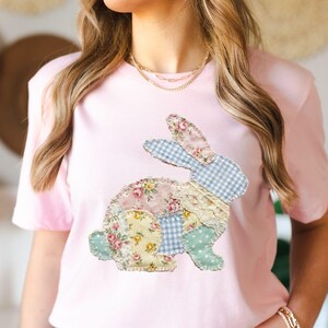 Op de afbeelding: Een lichtroze T-shirt met een patchwork konijnontwerp. Het konijn is gemaakt van diverse bloemen- en ruitjesstoffen in pasteltinten, waaronder roze, blauw, geel en groen. Het ontwerp is gecentreerd op de voorkant van het shirt.