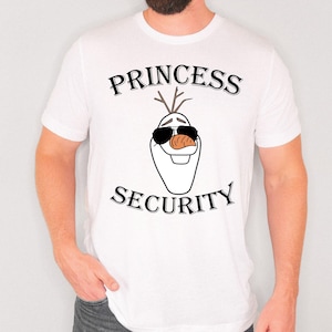 Pu&ograve; includere: T-shirt bianca con un'immagine a cartoni animati di Olaf di Frozen con occhiali da sole e un naso a carota. Il testo "PRINCESS SECURITY" &egrave; stampato sopra e sotto l'immagine in nero.