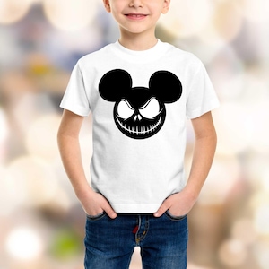 Puede incluir: Camiseta blanca con un gr&aacute;fico negro de una cara estilizada con orejas de Mickey Mouse y una sonrisa siniestra. El dise&ntilde;o est&aacute; centrado en la parte delantera de la camiseta. La camiseta la lleva un ni&ntilde;o.