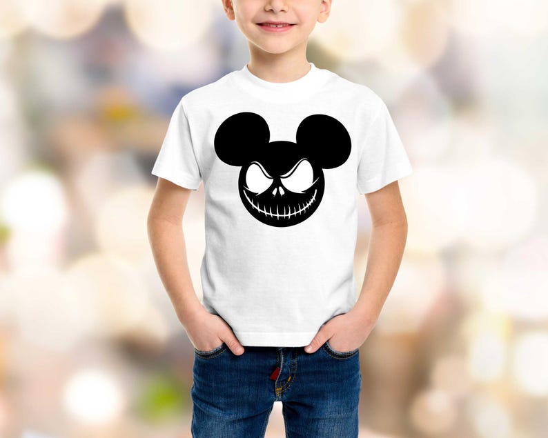 Puede incluir: Camiseta blanca con un gr&aacute;fico negro de una cara estilizada con orejas de Mickey Mouse y una sonrisa siniestra. El dise&ntilde;o est&aacute; centrado en la parte delantera de la camiseta. La camiseta la lleva un ni&ntilde;o.