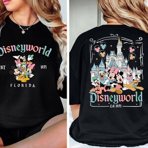 May include: Black long-sleeved top with a "Disneyworld" design in multiple colours on the front and back. The front graphic shows Mickey, Minnie, Donald, Daisy, and Goofy. The back graphic features the Disney castle and characters. "Est. 1971" is also displayed.