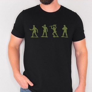 May include: Black t-shirt featuring a green silhouette of four toy soldiers in various poses. The graphic is centered on the chest. The shirt is made of a soft material and has short sleeves.