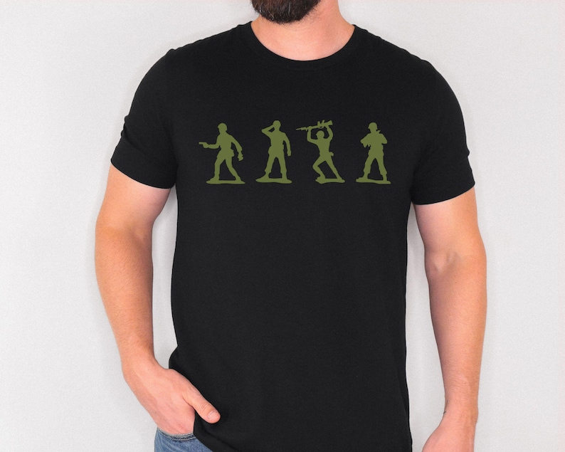 May include: Black t-shirt featuring a green silhouette of four toy soldiers in various poses. The graphic is centered on the chest. The shirt is made of a soft material and has short sleeves.