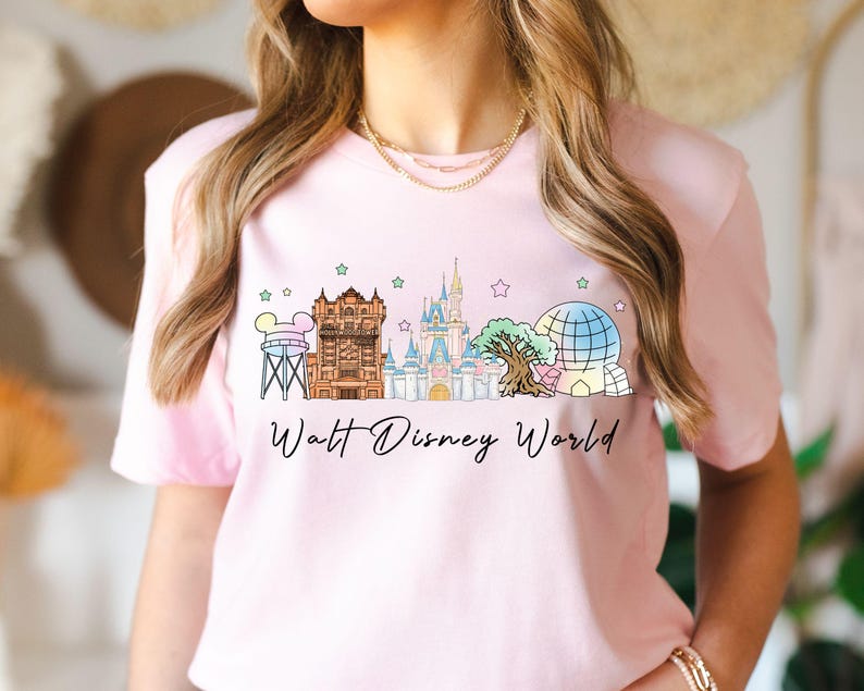 May include: A light pink t-shirt featuring a colorful graphic of Walt Disney World landmarks, including Cinderella Castle and Spaceship Earth. The words "Walt Disney World" are written in a script font below the graphic.