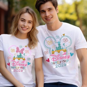 May include: White t-shirts with a colorful Disney design. The design includes a castle, fireworks, and the text "Disney Family Trip 2020". One shirt features a Minnie Mouse bow. The other shirt has a Mickey Mouse design.