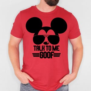 May include: A red short-sleeved t-shirt featuring a black graphic of a mouse silhouette wearing sunglasses. Below the graphic, the text reads TALK TO ME GOOF in bold black capital letters, flanked by two horizontal black lines on each side.