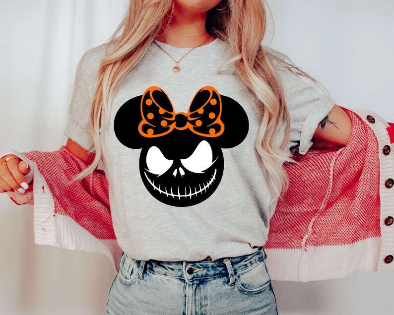 Puede incluir: Camiseta gris claro con una cabeza de Mickey Mouse negra con una cara de Jack Skellington y un lazo naranja con lunares. Dise&ntilde;o tem&aacute;tico de Halloween.