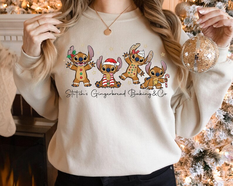 Puede incluir: Sudadera beige con un gr&aacute;fico de cuatro personajes Stitch estilo pan de jengibre con atuendos festivos. El texto "Stitch's Gingerbread Baking & Co" est&aacute; impreso debajo. La sudadera es de color neutro.